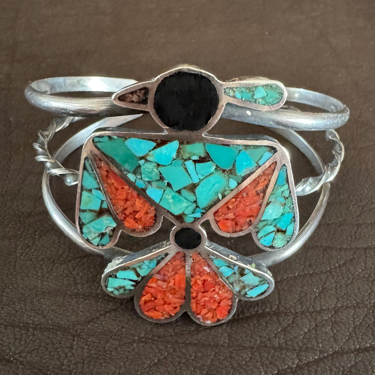 A sterling silver Native American cuff bracelet featuring turquoise and coral inlay, displayed on a brown textured leather background.
